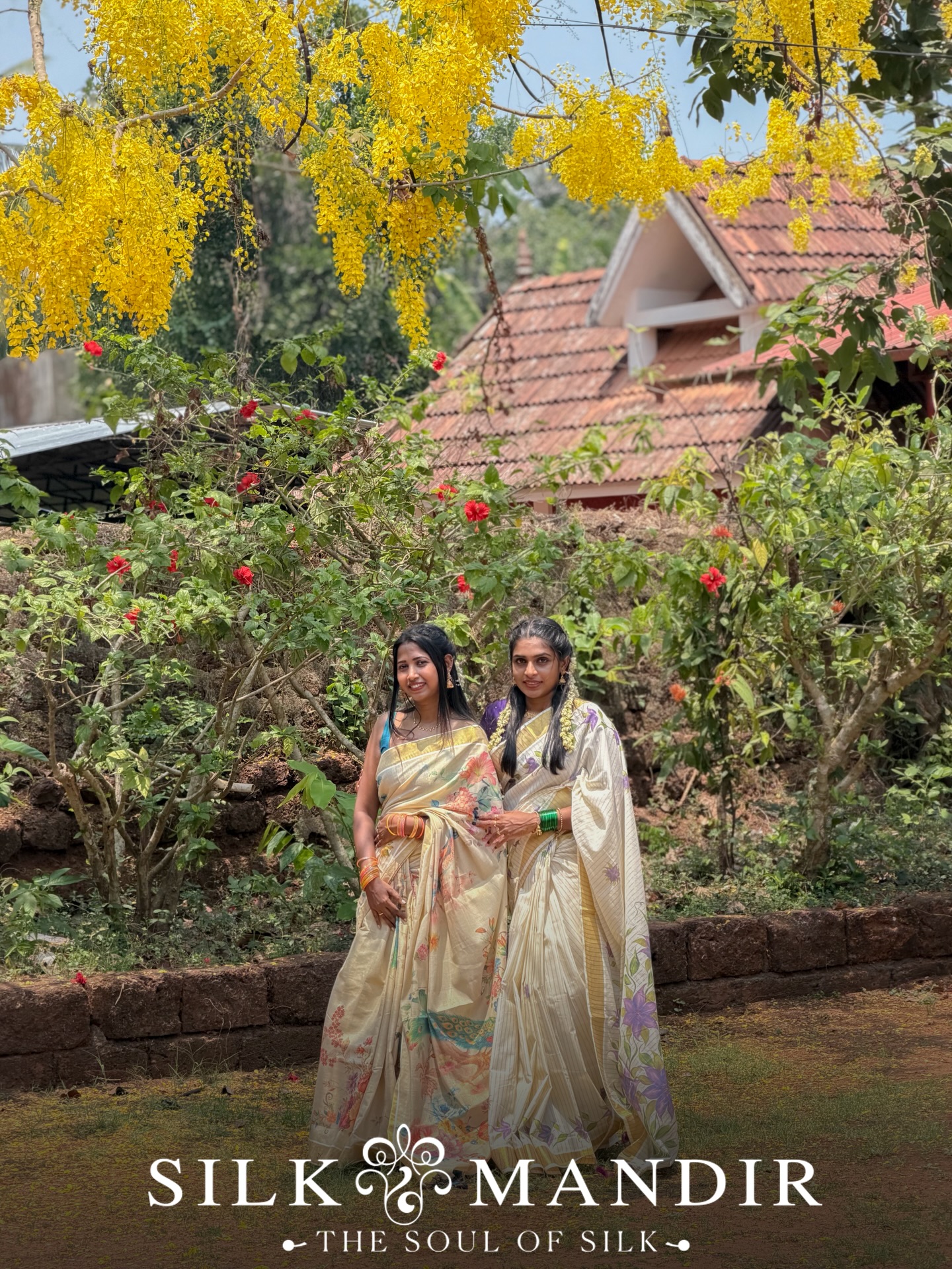 Two friends in kasavu sarees under a cassia tree