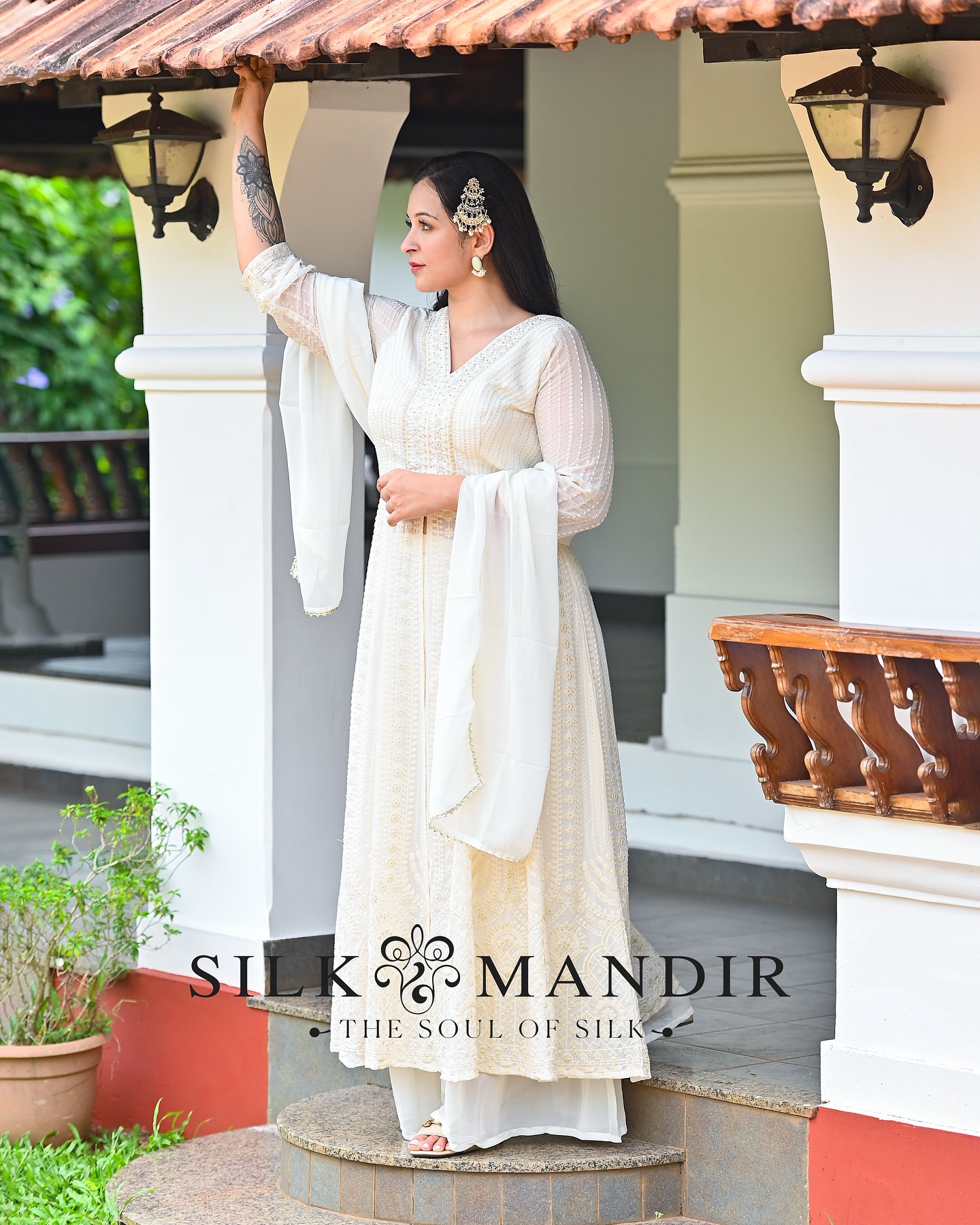 A woman in ivory chikankari anarkali standing on a Kerala home veranda with terracotta tile roof