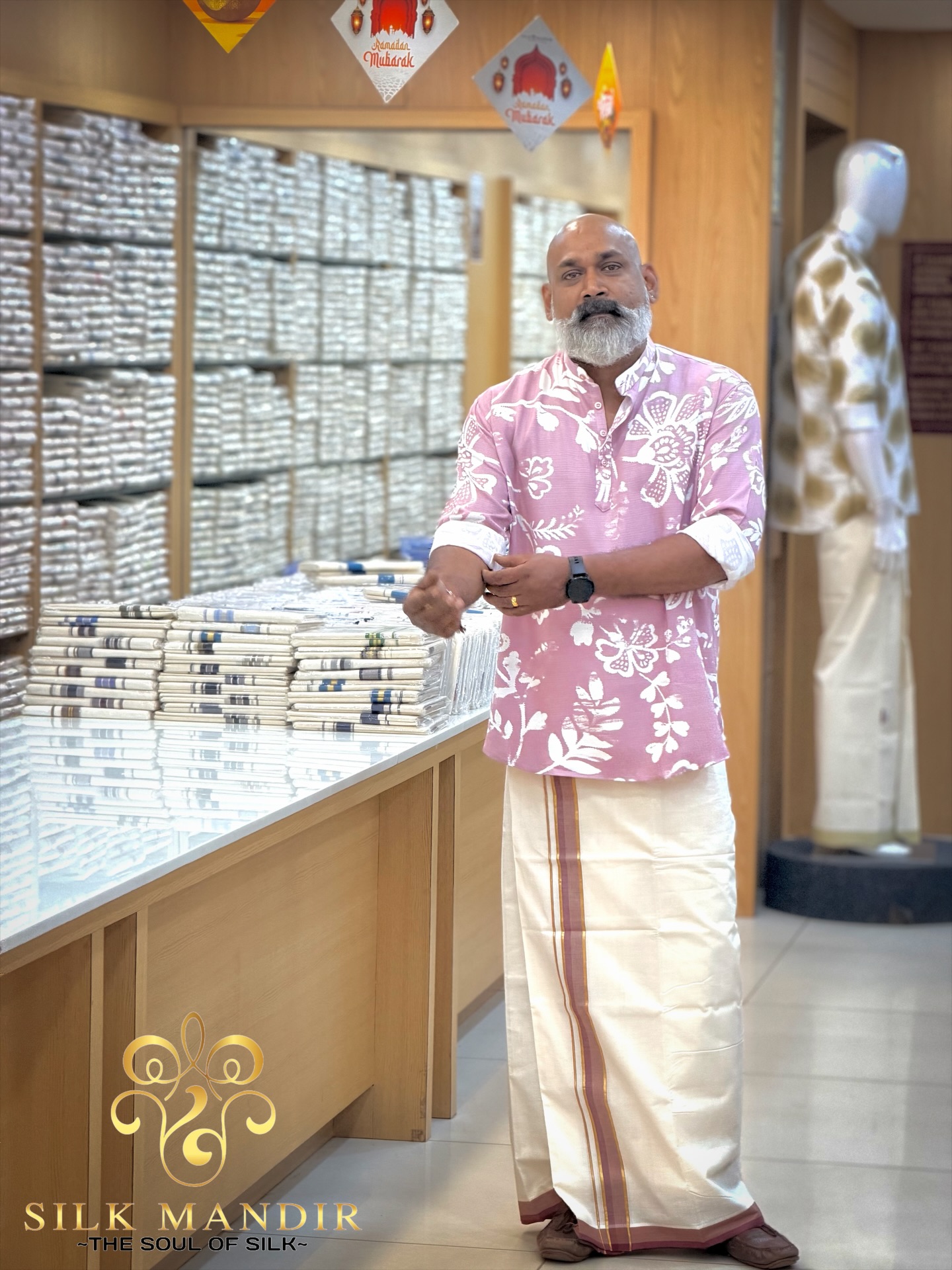 The owner of Silk Mandir, on the shop floor in a pink kurta and Kerala mundu